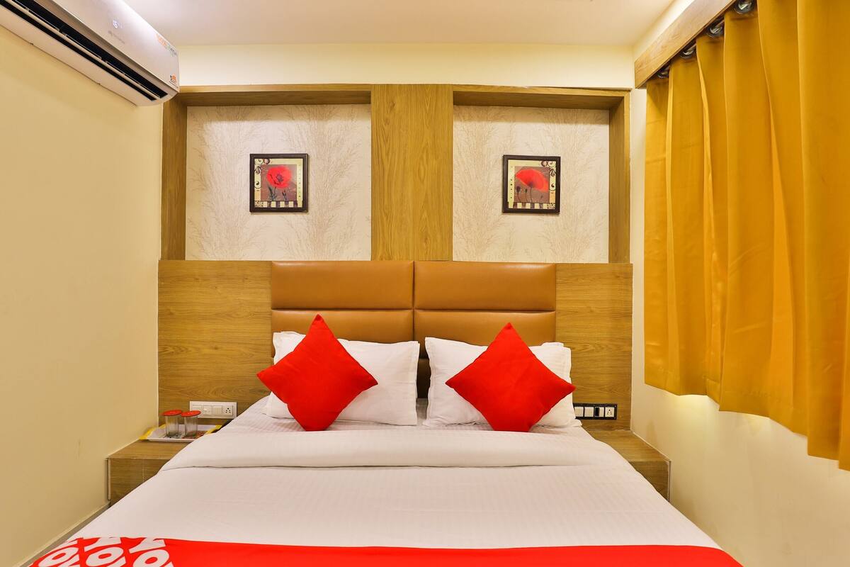 A hotel room with a wooden headboard, two red pillows, a white bedspread, and two framed pictures on the wall.