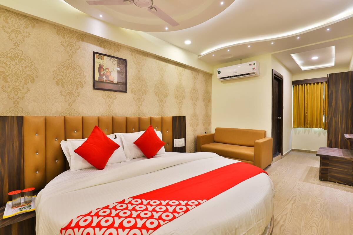 A hotel room with a large bed, a brown headboard, a brown sofa, and a small table.