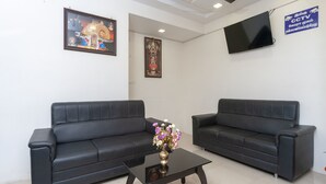 A reception area with two black leather sofas, a glass coffee table with a floral centerpiece, and a ceiling fan. - OYO 16595 Famous Residency (Tiruchirappalli)