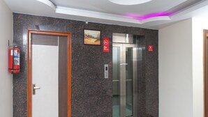 A modern elevator with a digital display, a fire extinguisher, and a door with a wooden frame. - OYO 16595 Famous Residency (Tiruchirappalli)