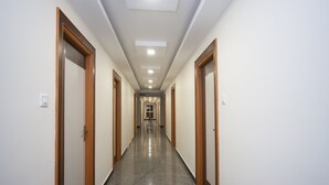 A long, narrow hallway with wooden doors on both sides, leading to a bright room at the end. - OYO 16595 Famous Residency (Tiruchirappalli)