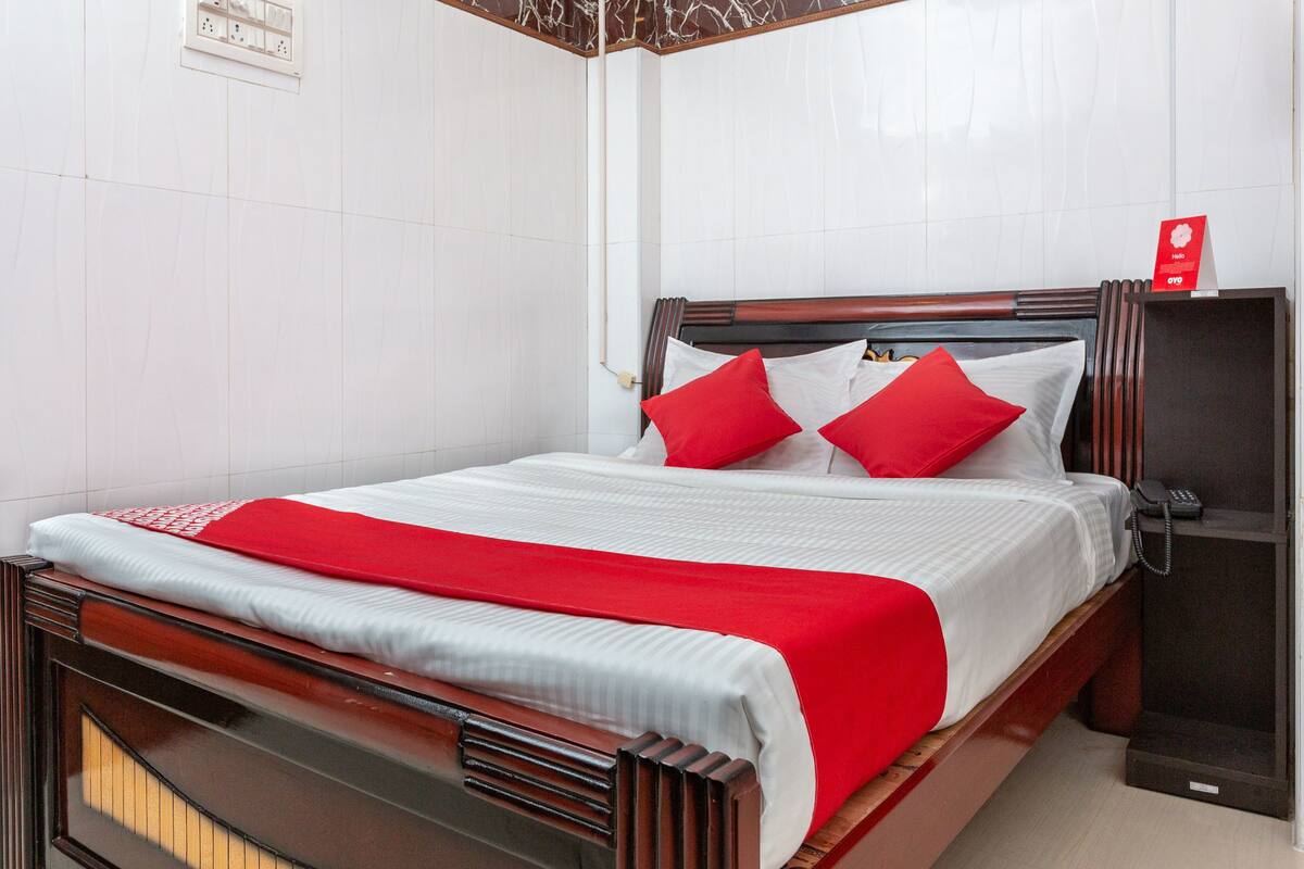 A neatly made bed with a red blanket and pillows, a wooden headboard, and a bedside telephone.