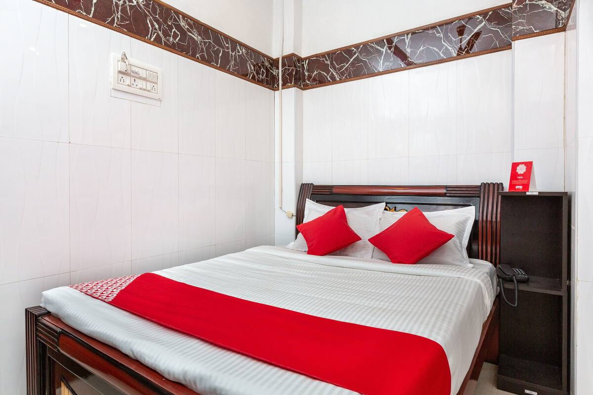 A hotel room with a bed, a wooden headboard, a red throw blanket, and a red sign on the wall.