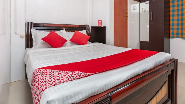 Una cama bien hecha con una colcha roja y blanca estampada, un cabecero de madera y dos almohadas rojas.