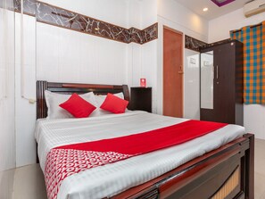 Una cama bien hecha con una colcha roja y blanca estampada, un cabecero de madera y dos almohadas rojas.