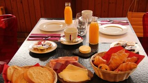 A breakfast table with plates, cups, and a variety of food items including bread, cheese, and pastries. - Hotel le Palladium (Champery)