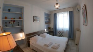 Een keurig opgemaakt slaapkamer met een bed, een bedlampje, planken en een raam met gordijnen.
