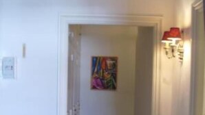 Een gang met een potplant, een schilderij aan de muur en een wandlamp.