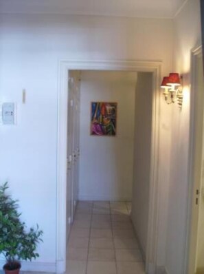 Un couloir avec une plante en pot, un tableau accroché au mur et un luminaire fixé au mur.