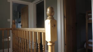 Un escalier en bois, doté d’une balustrade, mène à une pièce avec une porte en bois et un lit superposé.