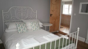 Une chambre avec un lit en métal blanc, une table ronde blanche et une porte en bois donnant sur un balcon.