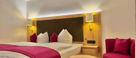 Una habitación de hotel con una cama grande, mesitas de noche, una pequeña mesa redonda y un sillón rojo.