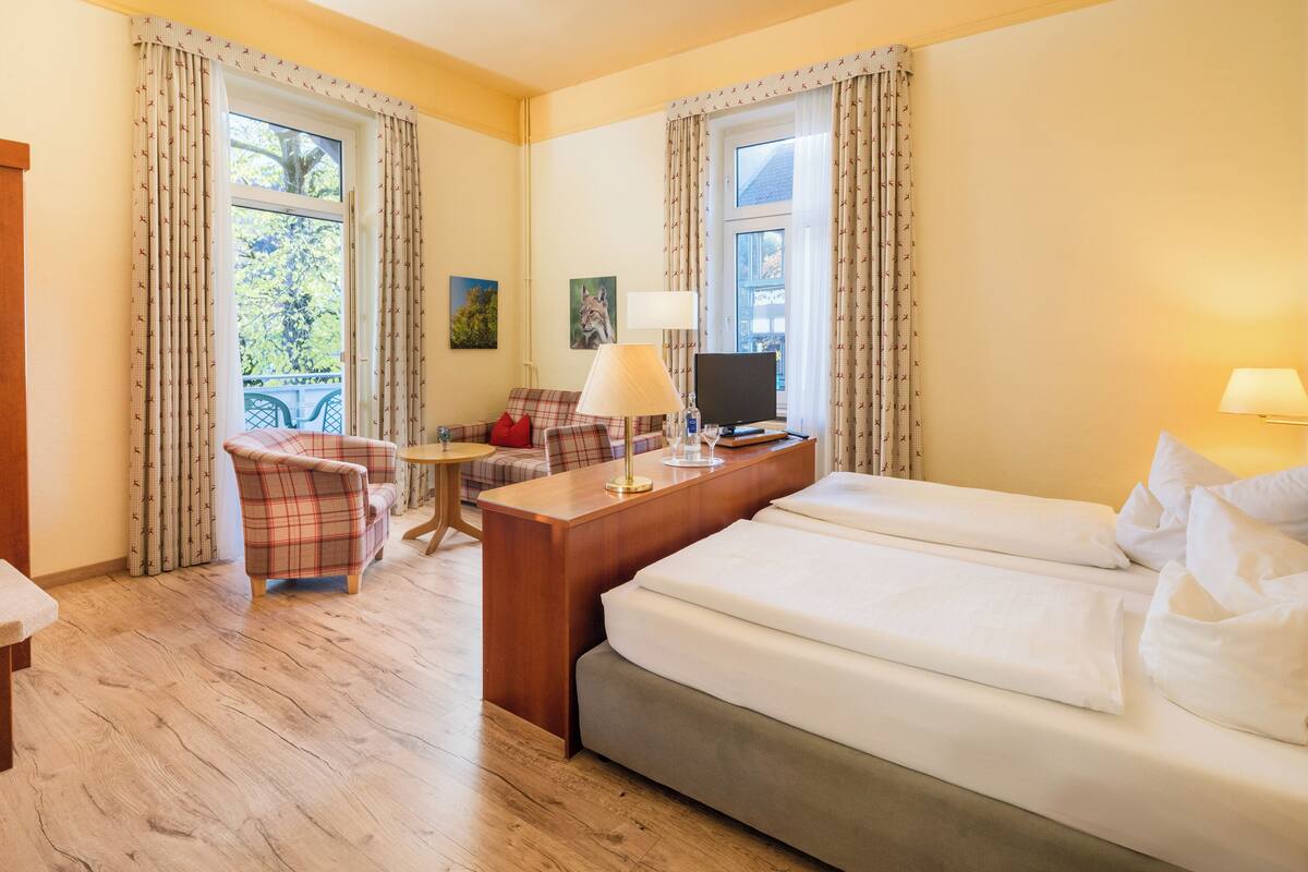Una habitación de hotel con una cama, un escritorio con televisor, una silla y una mesita.