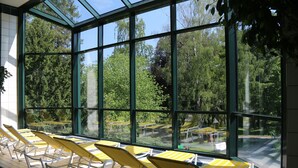 A sunlit room with large windows, rows of yellow chairs, and a view of a forested area.