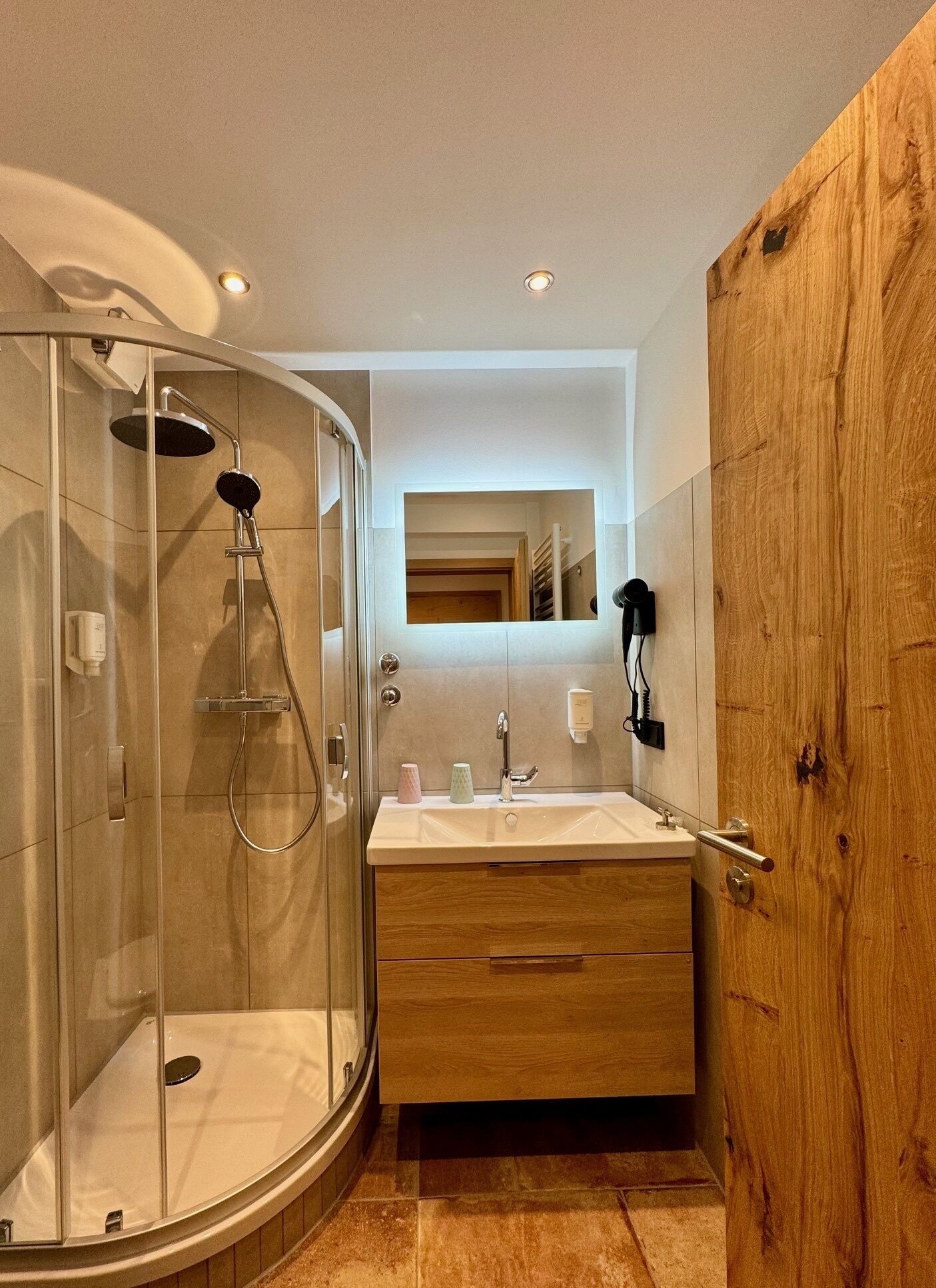 Un baño moderno con ducha envuelta en vidrio, tocador de madera y espejo sobre el lavamanos.