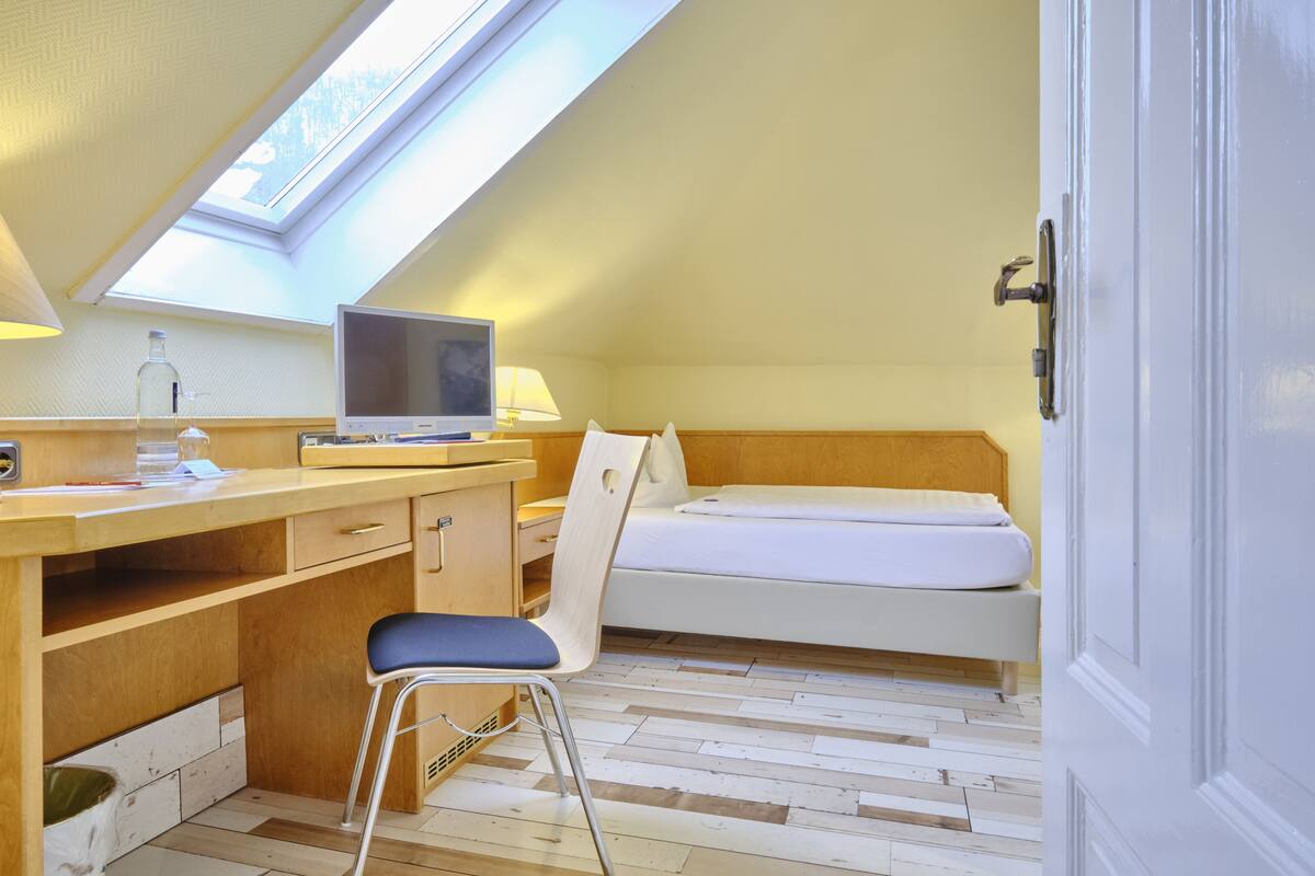 Una habitación tipo dormitorio con escritorio, silla, cama y tragaluz.