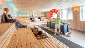 A sauna with wooden benches, a massage table, and a person holding an umbrella.