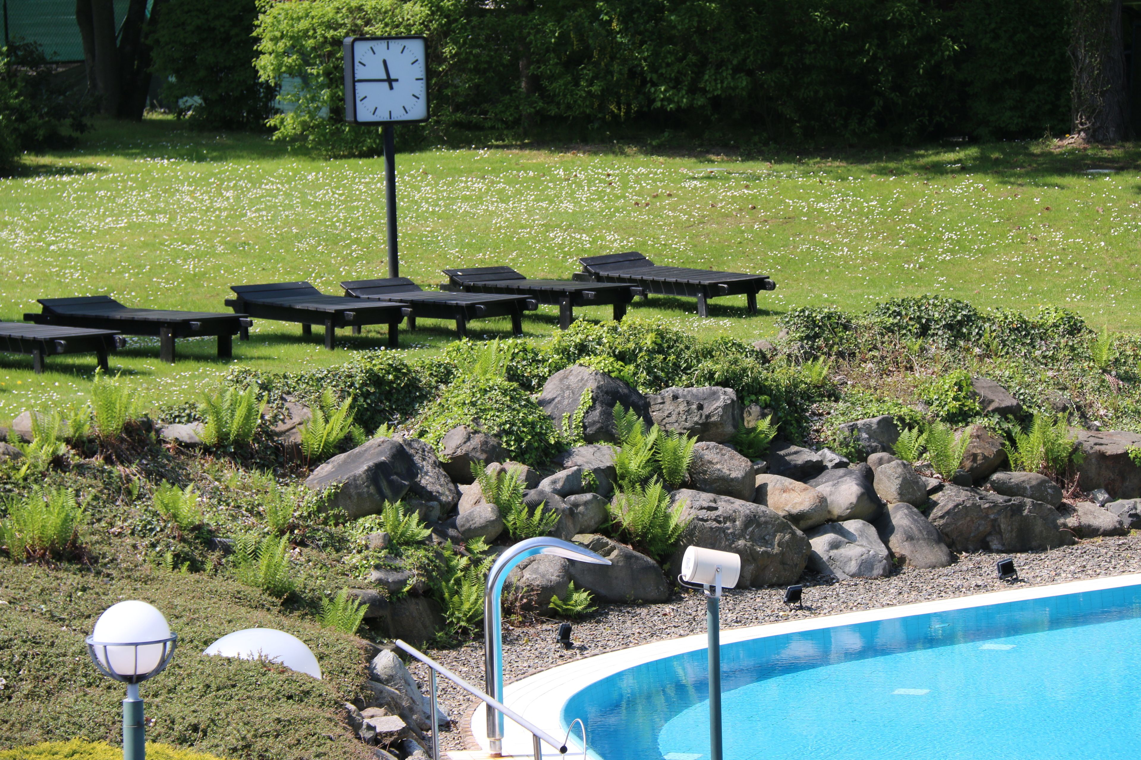 Zona de piscina con sillas de descanso, un reloj y un farol.