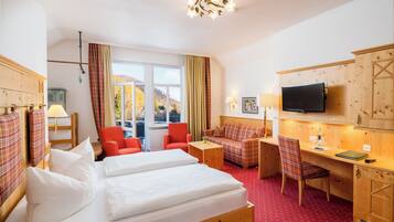 A hotel room with a bed, two red chairs, a sofa, a desk, a television, and a window with a view of mountains.