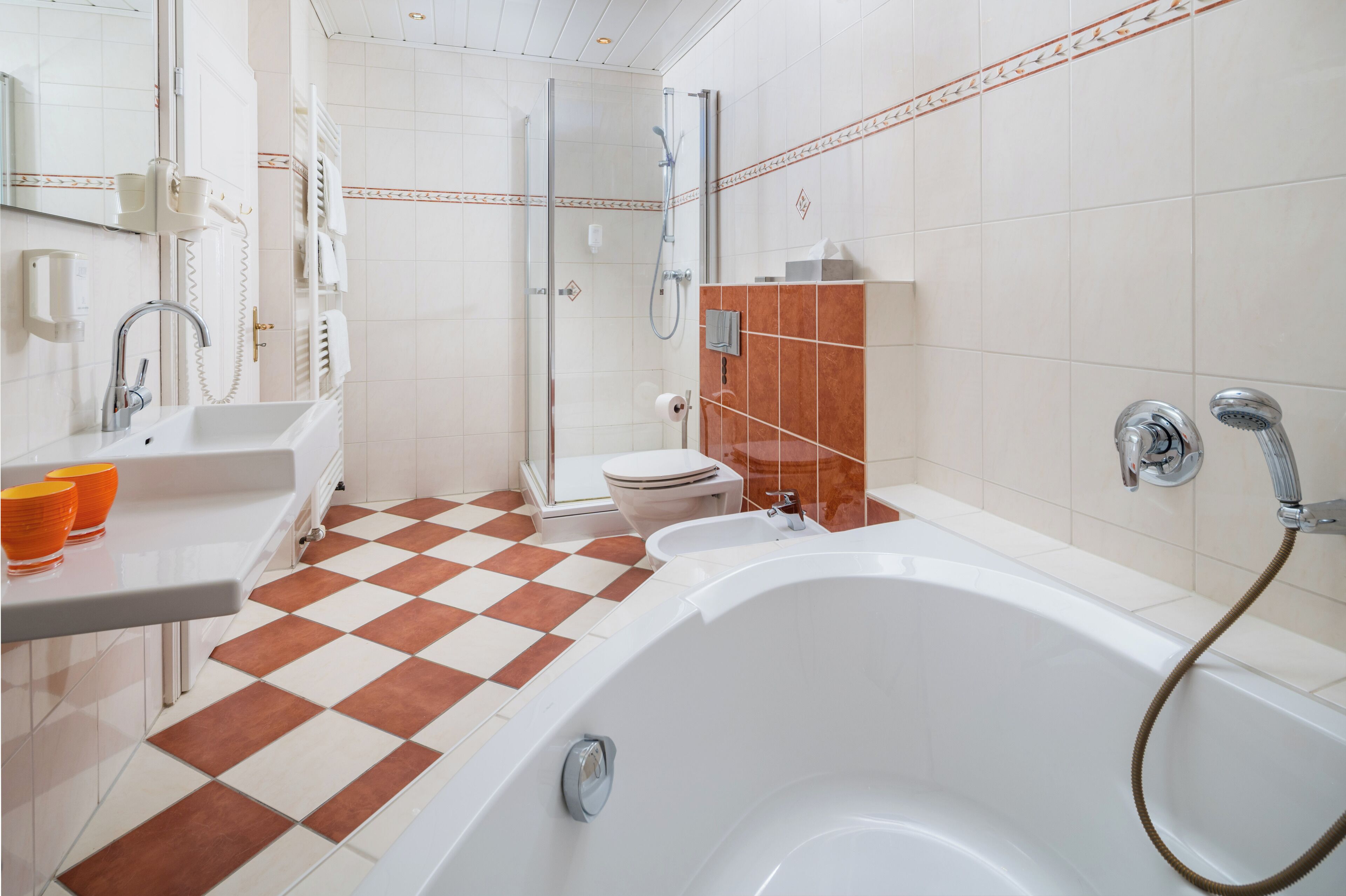 Ein Badezimmer mit Schachbrettboden, einer weißen Badewanne, einer Dusche und einem WC.