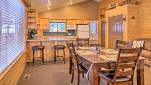 A cozy cabin-style kitchen with wooden cabinets, a central island, and a dining area with a table and chairs. - Bright & Cozy Duck Creek Cabin w/ Grill & Fire Pit (Duck Creek Village)