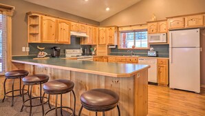 A kitchen with wooden cabinets, a central island with stools, a microwave, a refrigerator, and a dishwasher. - Bright & Cozy Duck Creek Cabin w/ Grill & Fire Pit (Duck Creek Village)