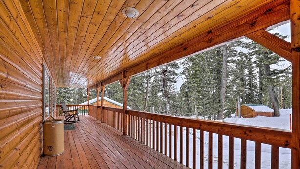 A wooden deck with a railing, a trash can, and a view of a snowy forest. - Bright & Cozy Duck Creek Cabin w/ Grill & Fire Pit (Duck Creek Village)