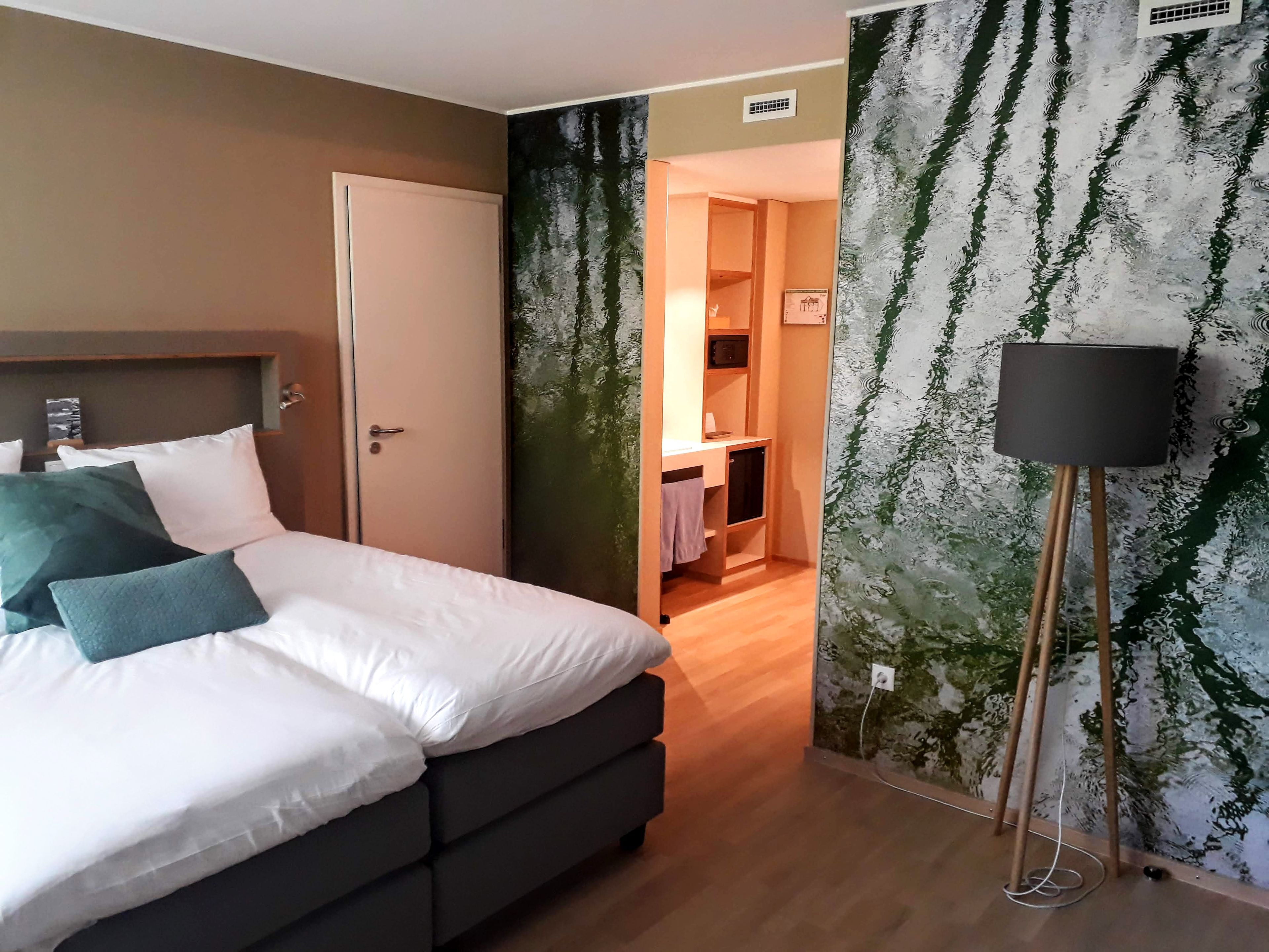 A bedroom with a bed, a bedside table, a lamp, and a view of a bathroom.