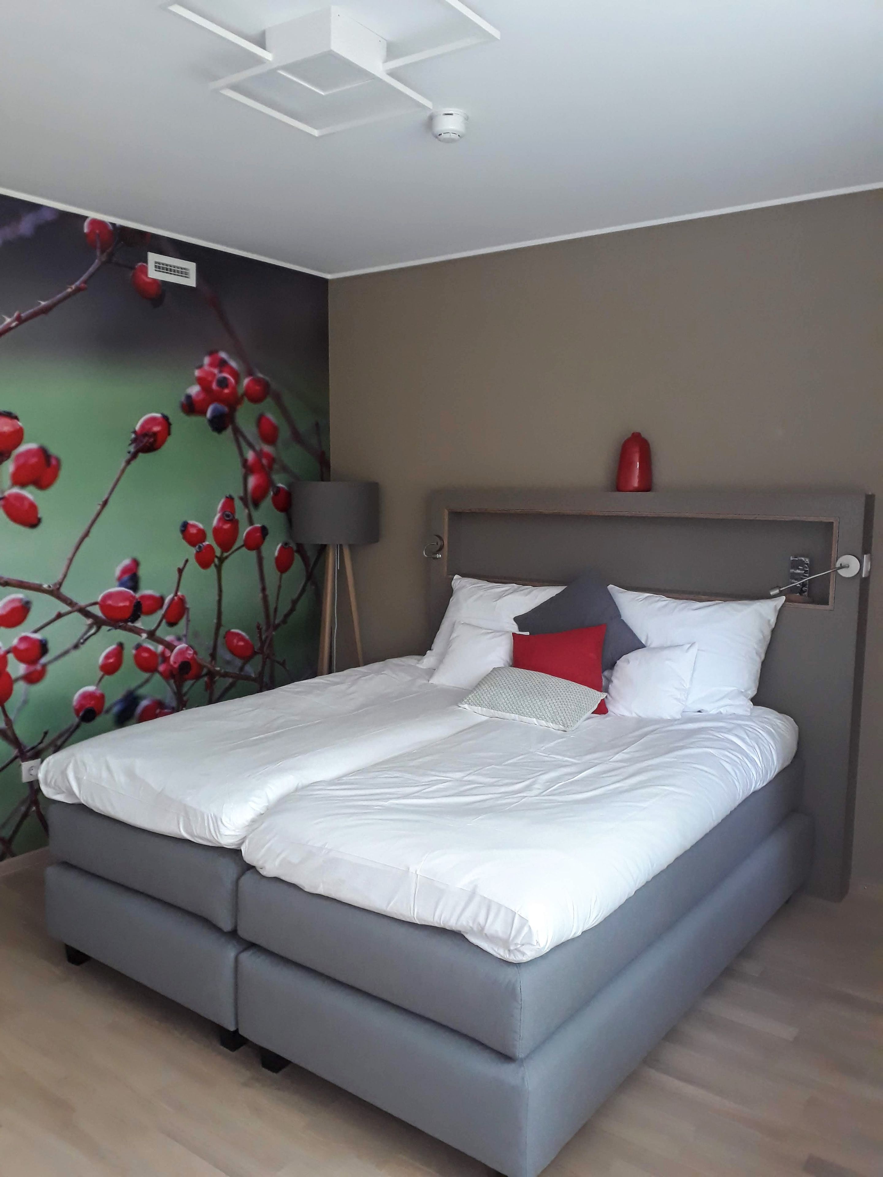 A modern bedroom with a bed, a headboard, a wall-mounted light, and a red decorative item.