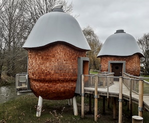 Dos estructuras en forma de cúpula con paredes de ladrillo y techo de metal, unidas por un puente de madera.