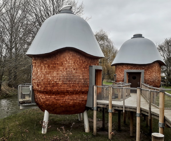 Two dome-shaped structures with brick walls and a metal roof, connected by a wooden bridge. - HôtelBrasserie & Ecolodges Péitche Lauer (Useldange)