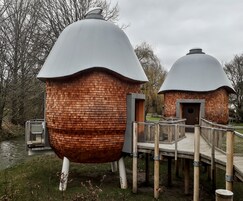 Dos estructuras en forma de cúpula con paredes de ladrillo y techo de metal, unidas por un puente de madera.