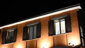 Eine Gebäudefassade bei Nacht mit drei Fenstern, jeweils mit Rollläden, beleuchtet durch Außenbeleuchtung.