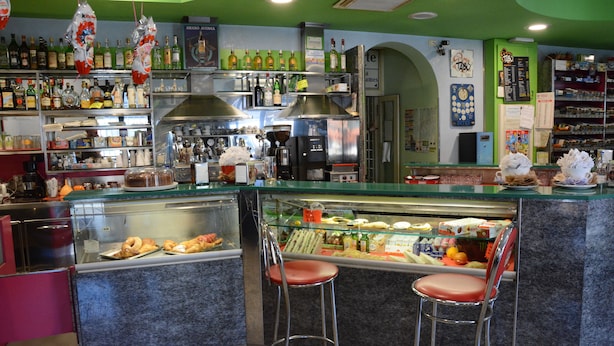 Eine Bar mit einer Auswahl an Gebäck in der Vitrine und verschiedenen Flaschen auf Regalen.