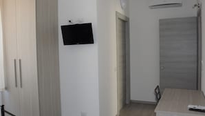Ein Zimmer mit Schrank, Wand-Fernseher, einer Tür und einem Tisch mit Fernbedienung.
