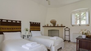 A hotel room with two beds, a fireplace, a window with shutters, and a small table with a vase. - Agriturismo di Serragiumenta (Altomonte)