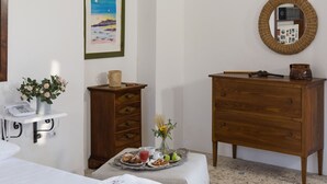A hotel room with a bed, a bedside table with a phone, a wooden dresser, a tray with breakfast items, a vase with flowers, and a framed picture on the wall. - Agriturismo di Serragiumenta (Altomonte)