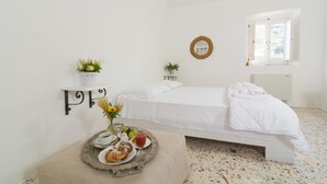 A clean, white room with a bed, a small table with breakfast items, a window, and a wall-mounted mirror. - Agriturismo di Serragiumenta (Altomonte)