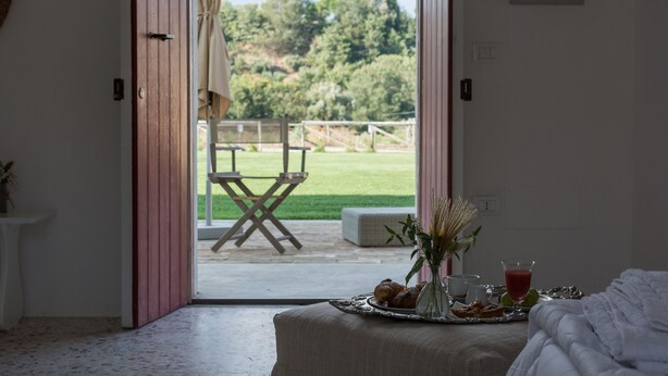 A room with a bed, a table with breakfast items, and a view of a grassy outdoor area through an open door. - Agriturismo di Serragiumenta (Altomonte)