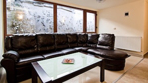 A modern living room with a leather sectional sofa, a glass coffee table, and a view through large windows. - Pensiunea Schwartz (Cluj-Napoca)