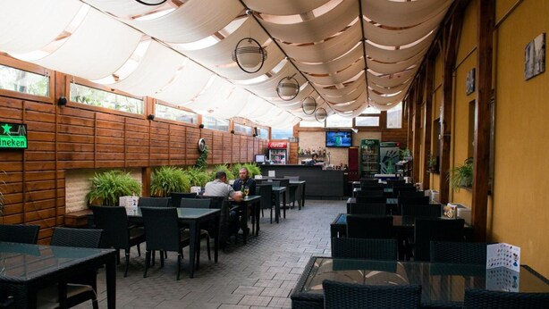 An outdoor cafe with wooden tables and chairs, a Coca-Cola refrigerator, and a Heineken sign. - Pensiunea Schwartz (Cluj-Napoca)