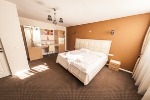 A hotel room with a large bed, a desk, a chair, a wardrobe, and a mirror.