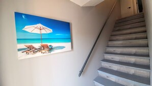 Een trap met een leuning die uitkomt op een plateau, waar een schilderij van een strandscène aan de muur hangt.