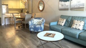 Een woonkamer met een blauwe bank, een rond bijzettafeltje en een eethoek met een houten tafel en stoelen.