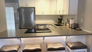 Een moderne keuken met witte kasten, een roestvrijstalen koelkast, een dubbele spoelbak en een inbouw kookeiland met krukken.
