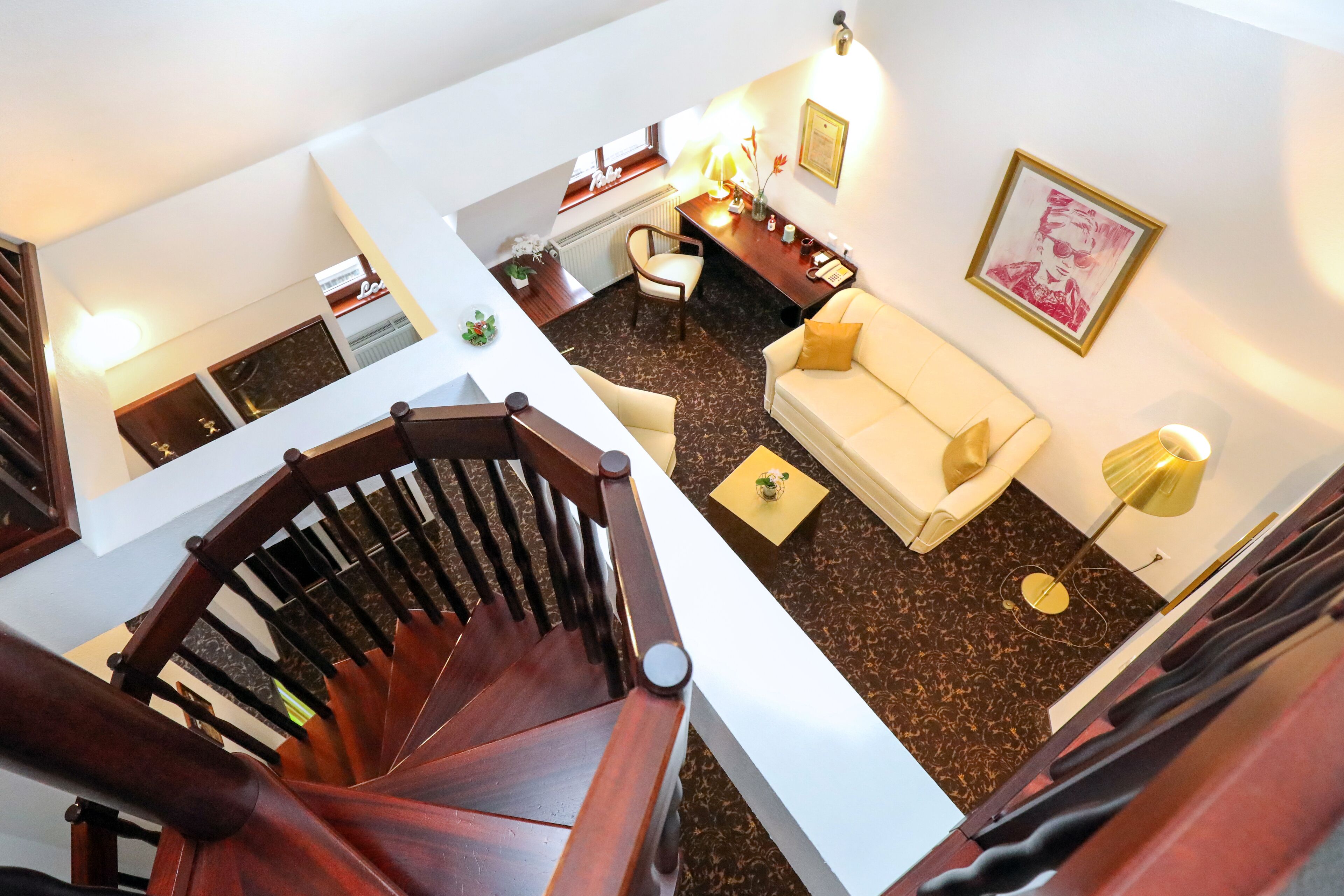 Ein mehrgeschossiges Interieur mit Treppe, einem Wohnbereich mit Sofa und Sesseln, einem Esstisch und einer Küchenzeile.
