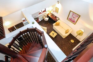 Un interior de varios niveles con una escalera, una sala de estar con sofá y sillones, una mesa de comedor y una zona de cocina.