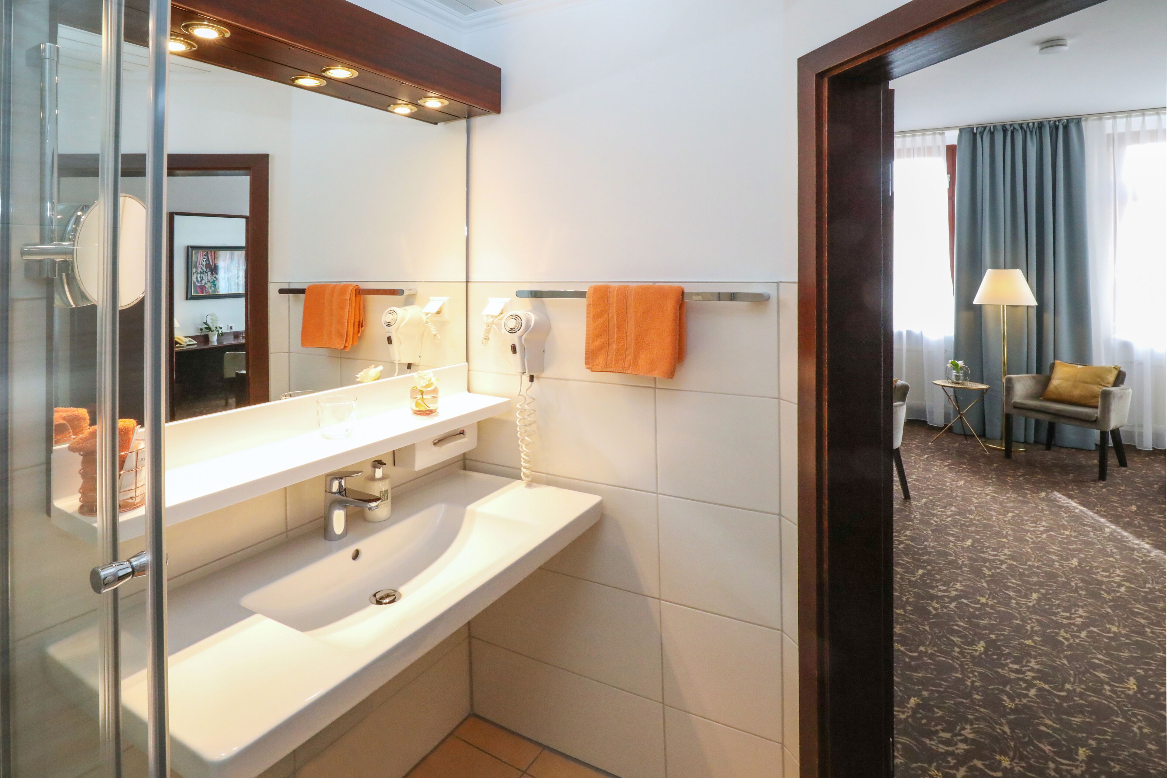 A modern bathroom with a large mirror, white sink, and a hairdryer on the wall.