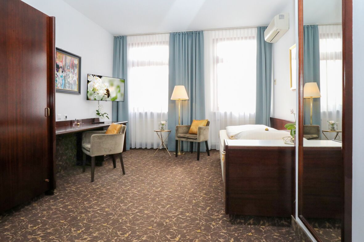 Ein Hotelzimmer mit Schreibtisch, Stuhl, zwei Lampen, einem Bett und einem großen Spiegel.