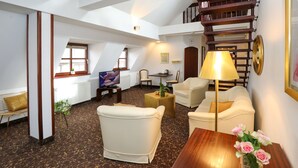 A spacious living room with a high ceiling, a wooden staircase, and a cozy seating area with a sofa and armchairs. - City-Hotel Aschaffenburg (Aschaffenburg)